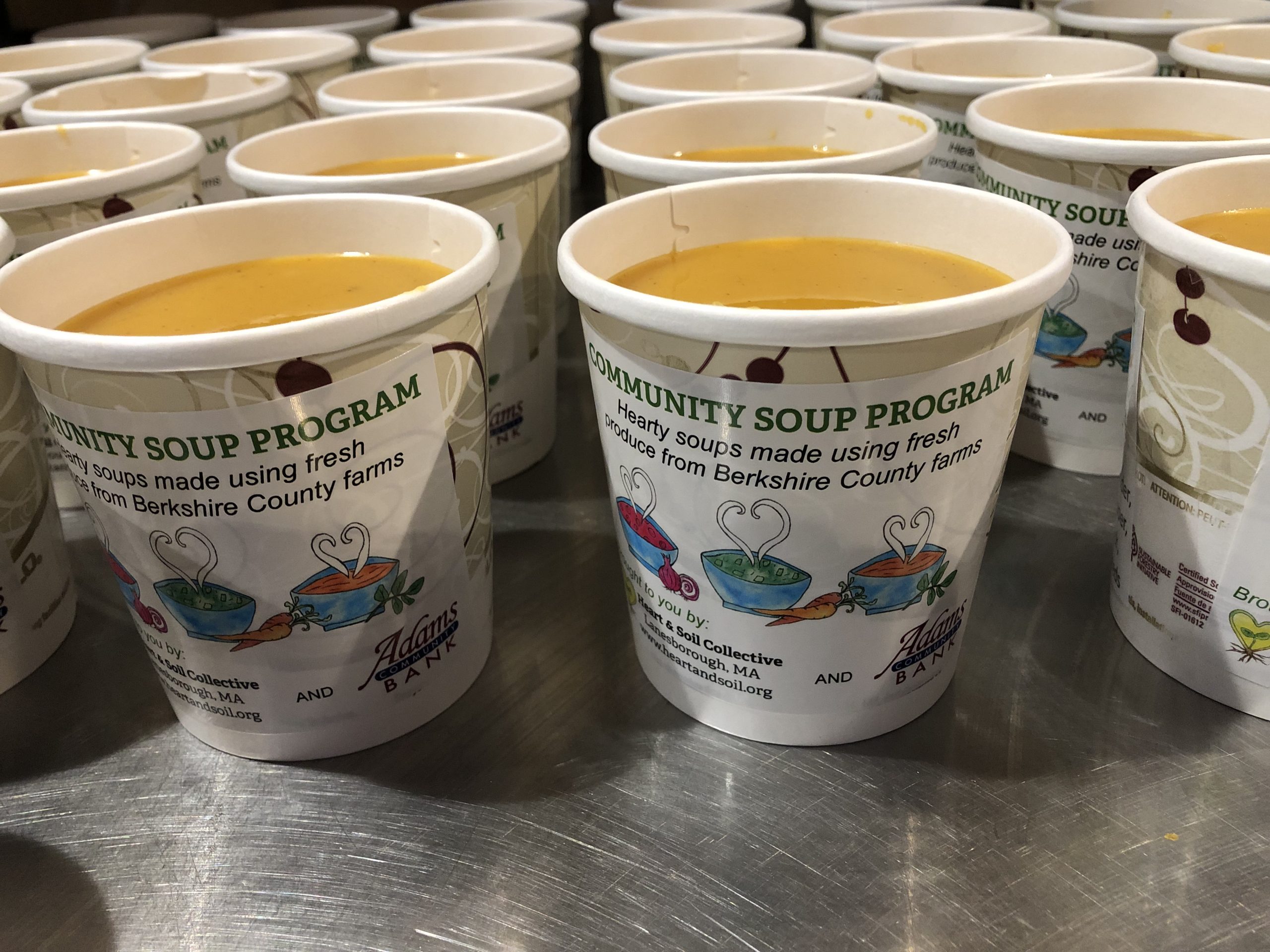 Rows of community soup program containers filled with freshly made soup, labeled with local farm information.