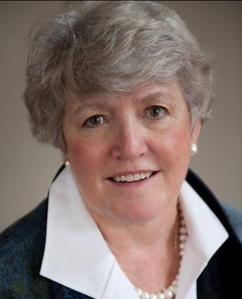 Portrait of Abbie Von Schlegell, wearing a white collared shirt, a pearl necklace, and a dark blazer, smiling at the camera.