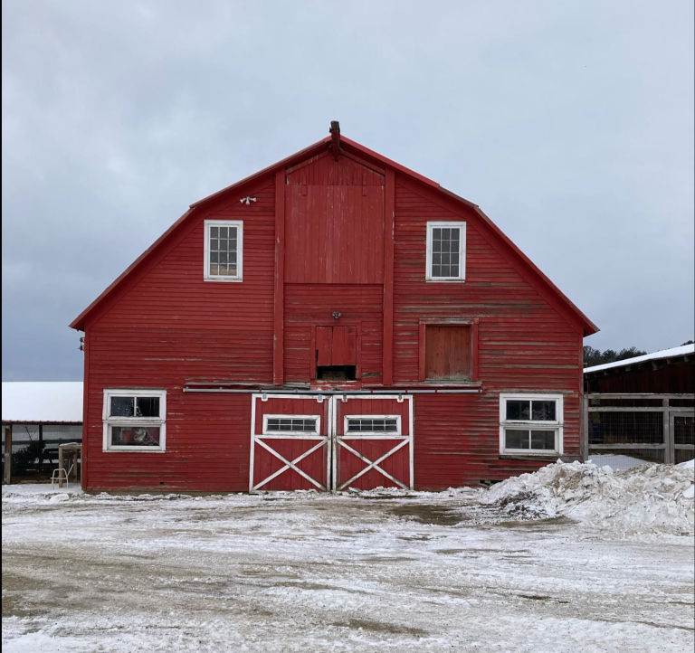 A large red barn with white trim standing in a snowy rural landscape under an overcast sky.