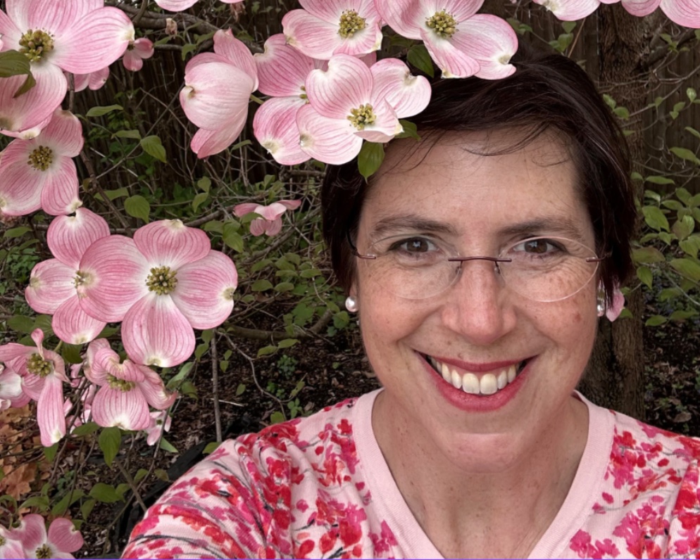 Jennifer Zaslow in glasses smiling in front of a tree covered in pink dogwood flowers.