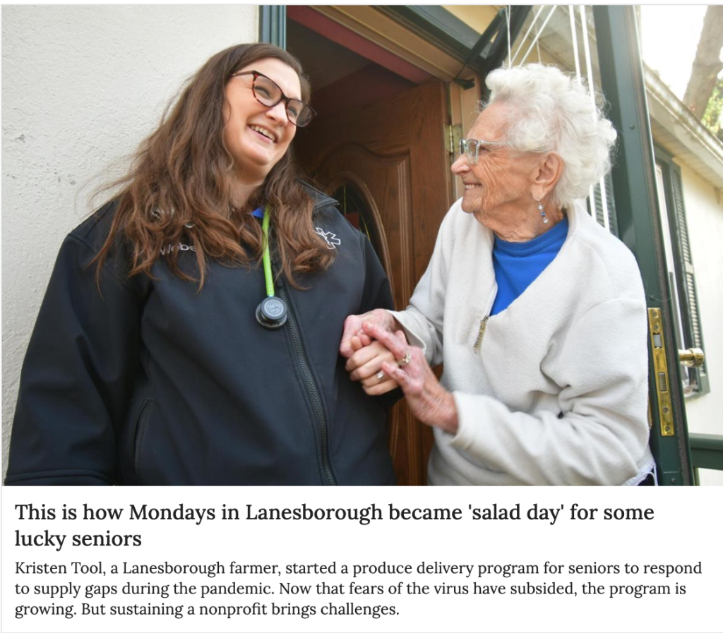 A smiling woman in a black jacket holds hands with an elderly woman in a white fleece, illustrating a produce delivery program for seniors in Lanesborough.